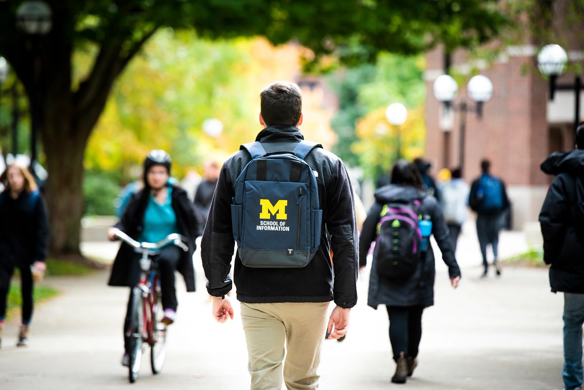A student wears a UMSI backpack in fall on the drag.